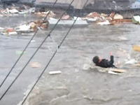 津波の新しい動画。濁流の中で必死に電線に掴まって助かった人と建物の上に乗って流される人