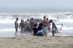 お盆休みの大洗海岸でハイエースを埋める遊びをしている若者たちが撮影される。